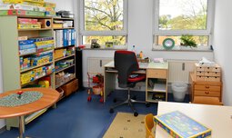 Spiel- und Arbeitszimmer mit Schreibtisch und Regal mit Spielen | © Caritasverband der Erzdiözese München und Freising e.V.
